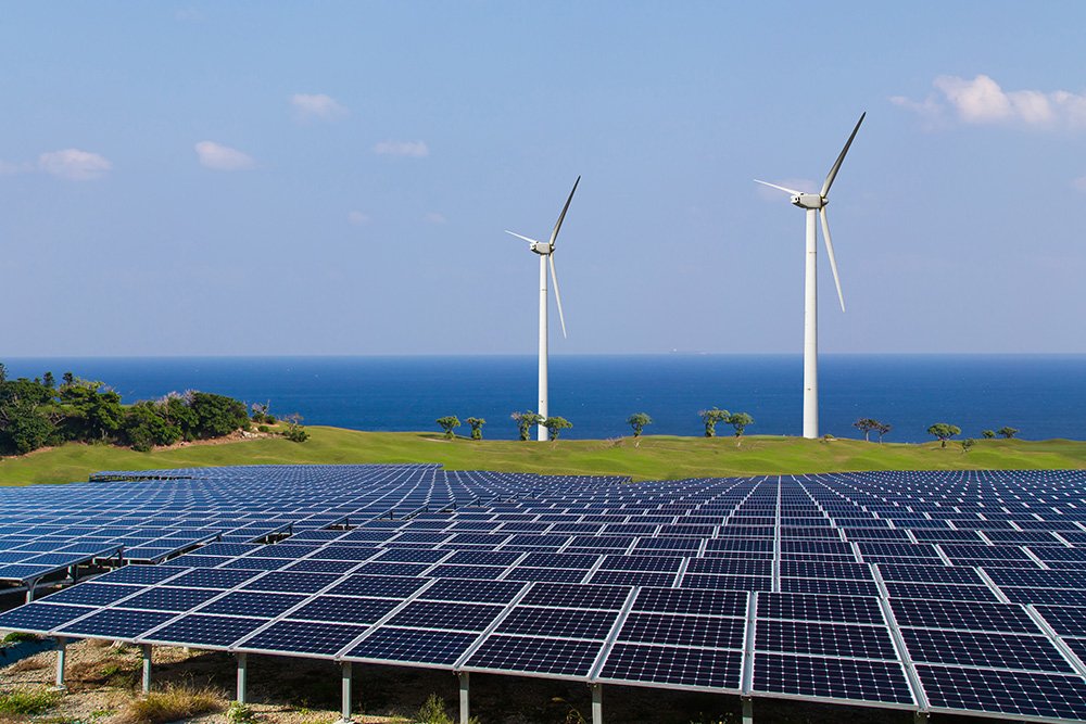 Zwei Windkraftanlagen mit Sonnenkollektoren im Vordergrund und dem Meer dahinter